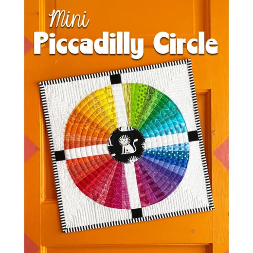 Mini Piccadilly Circle Titelbild Runder Mini-Quilt im Regenbogen-Fächermuster mit schwarzem Mittelkreis und Löwen-Applikation, aufgehängt an einer orangefarbenen Holztür.